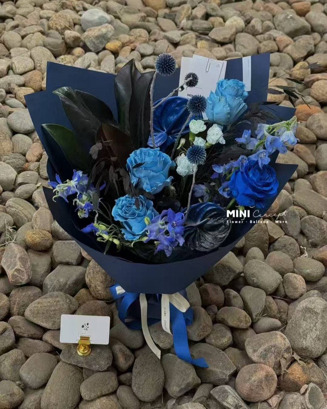 Bouquet of blue flowers in a black container on pebbles